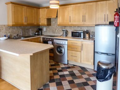 A kitchen with wooden cabinets a washing machine a microwave and a refrigerator at Apartment One in Duncannon County Wexford