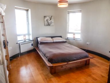 A bedroom with a double bed between two windows with lamps on the windowsills at Apartment One in Duncannon County Wexford