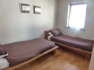 A bedroom with two single beds with brown bedding and wooden frames and a window with blinds at Apartment One in Duncannon County Wexford
