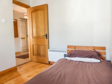 A bedroom with a wooden bed and an open wooden door showing a hallway at Apartment One in Duncannon County Wexford