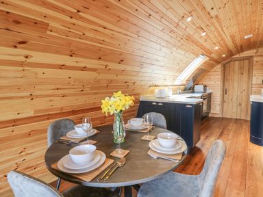 A dining area with a round table set for four and a kitchen with wooden walls and ceiling at Bluebell in St Harmon near Rhayader
