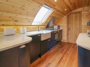 A kitchen with wooden walls and ceiling a skylight window a white countertop dark cabinets a toaster kettle oven microwave and wooden floor at Bluebell in St Harmon near Rhayader
