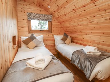 A small bedroom with two single beds wood paneled walls and a window at Bluebell St Harmon near Rhayader