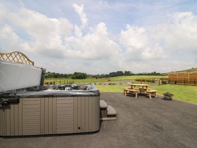 An outdoor area with a hot tub benches a picnic table and a fire pit overlooking fields and hills at Bluebell in St Harmon near Rhayader