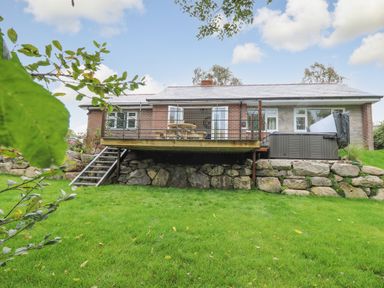 A house with a raised wooden deck and stairs leading to a grassy yard at Ger Yr Afon Cottage in St Harmon near Rhayader