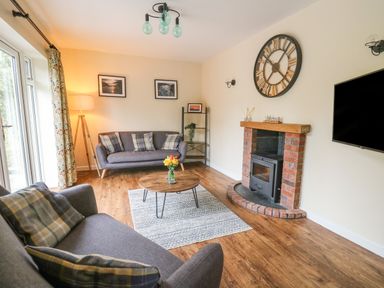 A living room with two sofas a wooden coffee table a brick fireplace and a wall clock at Ger Yr Afon Cottage in St Harmon near Rhayader