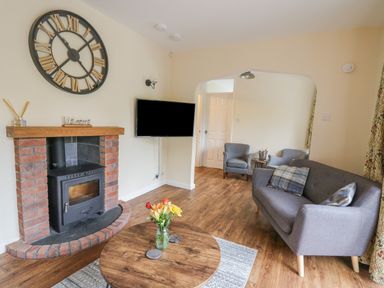 A living room with a wood burning stove a wall clock a sofa and two armchairs at Ger Yr Afon Cottage in St Harmon near Rhayader