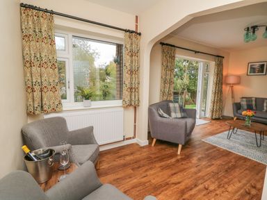 A living room with gray armchairs patterned curtains a coffee table with flowers and wooden flooring at Ger Yr Afon Cottage in St Harmon near Rhayader