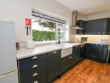A kitchen with dark cabinets a white countertop a sink under a window and appliances at Ger Yr Afon Cottage in St Harmon near Rhayader