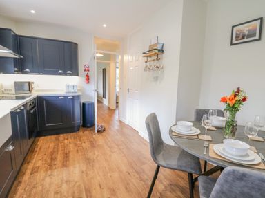 A kitchen with dark cabinets a round dining table set with plates glasses and flowers at Ger Yr Afon Cottage in St Harmon near Rhayader