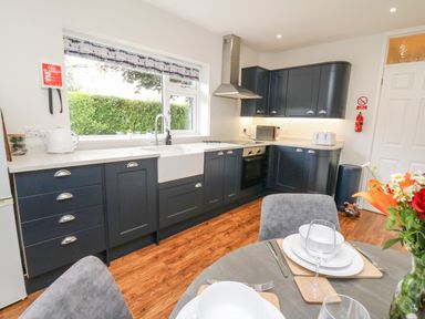A kitchen with dark cabinets white countertops stainless steel appliances and a dining table set with plates glasses and cutlery at Ger Yr Afon Cottage in St Harmon near Rhayader