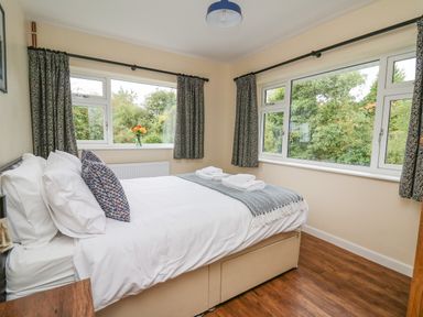 A bedroom with a double bed near two windows and wooden floor at Ger Yr Afon Cottage in St Harmon near Rhayader