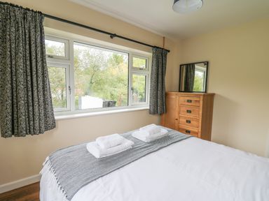 A bedroom with a bed with towels on it a window with curtains and a wooden chest of drawers with a mirror at Ger Yr Afon Cottage in St Harmon near Rhayader