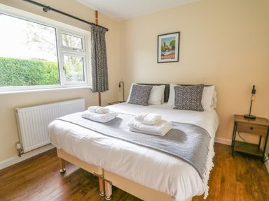 A bedroom with a bed made with white linens and towels on it a window with curtains and a framed picture on the wall in Ger Yr Afon Cottage St Harmon near Rhayader