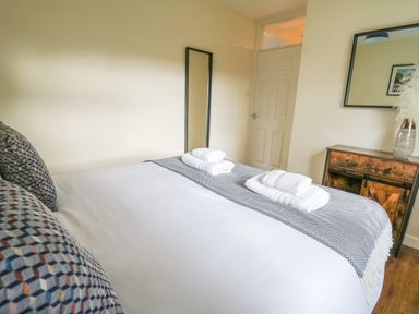 A bedroom with a bed with folded towels pillows and a blanket a mirror and a wooden cabinet with a vase at Ger Yr Afon Cottage in St Harmon near Rhayader