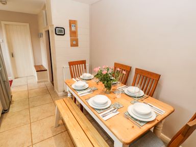 A dining area with a wooden table set for six people with chairs and a bench and a vase of flowers at The Old Bakery in Milton Tenby