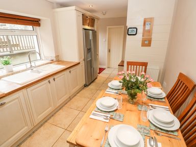 A kitchen with a dining table set for six with dishes and flowers at The Old Bakery in Milton Tenby