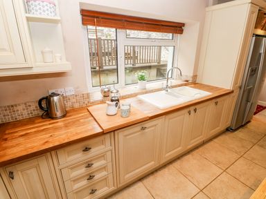 A kitchen with wooden countertops a sink a kettle cups and a window with blinds at The Old Bakery in Milton Tenby