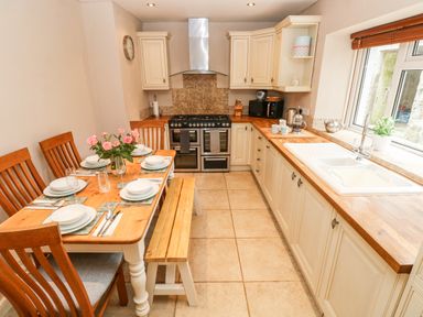A kitchen with a wooden dining table set for six and cream cabinets at The Old Bakery in Milton Tenby