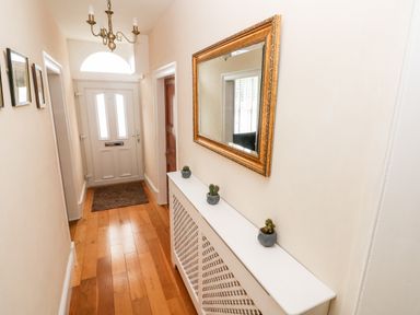 A hallway with a white radiator cover with three small plants a large gold-framed mirror wooden floor and a white front door at The Old Bakery in Milton Tenby