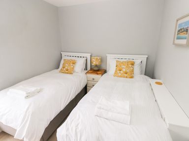 A bedroom with two single beds white bedding yellow pillows a small wooden nightstand and a lamp at The Old Bakery in Milton Tenby