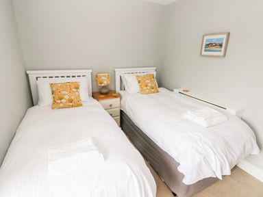 A bedroom with two single beds with white bedding and yellow patterned pillows at The Old Bakery in Milton Tenby