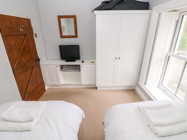 A bedroom with two single beds with white linens towels on them a wooden door white wardrobe small television on a white cabinet and a window at The Old Bakery in Milton Tenby
