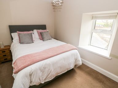 A bedroom with a bed with pillows and a blanket beside a window at The Old Bakery in Milton Tenby