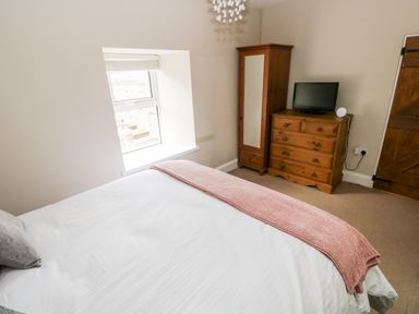 A bedroom with a bed a window a wooden wardrobe and a dresser with a television at The Old Bakery in Milton Tenby