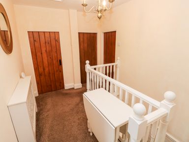 A hallway with three wooden doors a white folding table white railing and a circular wall mirror at The Old Bakery in Milton Tenby