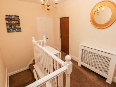 A hallway with white banister, brown door, white double doors, radiator cover and round mirror at The Old Bakery in Milton Tenby