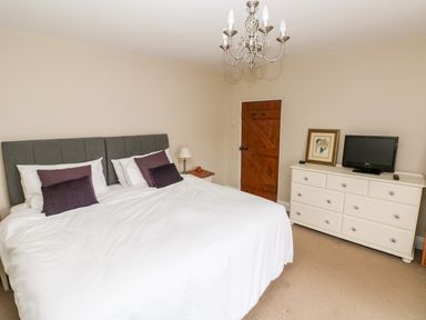 A bedroom with a double bed white dresser and chandelier at The Old Bakery in Milton Tenby