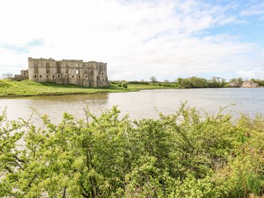 A large stone castle by a river with greenery in the foreground at The Old Bakery in Milton Tenby