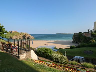 A garden with flower beds benches and a fenced area overlooking a sandy beach and the sea at The Old Bakery in Milton Tenby