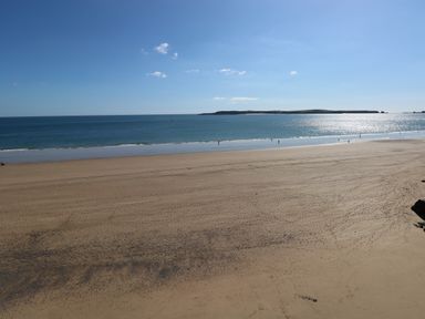 A sandy beach with footprints and the sea with a clear sky at The Old Bakery in Milton Tenby