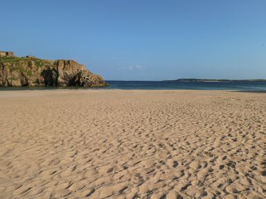 A sandy beach with rocky cliffs on the left and the ocean in the background at The Old Bakery in Milton Tenby