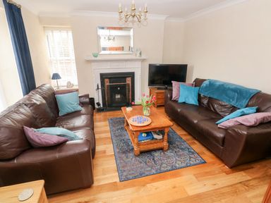 A living room with two brown leather sofas a wooden coffee table with flowers a fireplace and a television at The Old Bakery in Milton Tenby