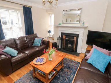 A living room with brown leather sofas a wooden coffee table with flowers a fireplace and a television at The Old Bakery in Milton Tenby