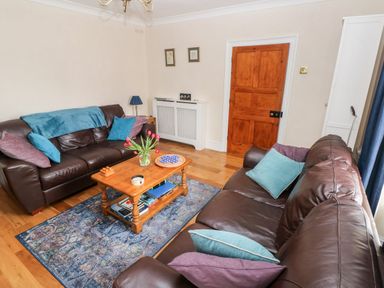 A living room with brown leather sofas and a wooden coffee table with flowers at The Old Bakery in Milton Tenby