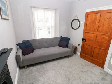 A small room with a gray sofa and pillows a wooden door and a window with blinds at The Old Bakery in Milton Tenby