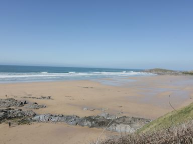 A sandy beach with rocks and ocean waves under a clear sky at Fistral Drift in Newquay