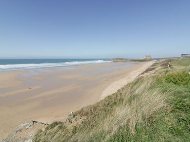 A sandy beach with ocean waves and grassy dunes at Fistral Drift in Newquay