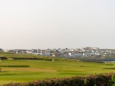 A view of a town behind green fields and a hedge at Fistral Drift in Newquay