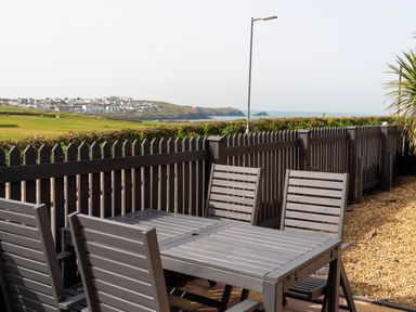 An outdoor patio with a wooden table and chairs next to a picket fence overlooking a coastal town and sea at Fistral Drift in Newquay