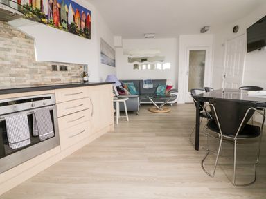 A kitchen and living area with oven and cabinets sofa and glass coffee table and dining table with chairs at Fistral Drift in Newquay