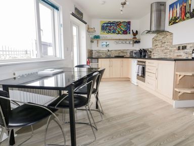 A kitchen with light wood cabinets a black dining table with black chairs and colorful wall art at Fistral Drift in Newquay