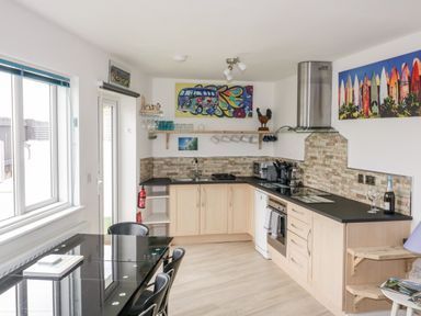 A kitchen with wooden cabinets black countertops dining table with chairs and colorful wall art at Fistral Drift in Newquay