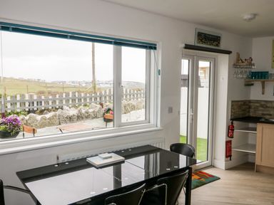 A dining area with a black glass table and chairs next to large window and glass doors leading outside at Fistral Drift in Newquay