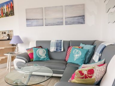 A living room with a sectional sofa with colorful cushions and glass coffee table at Fistral Drift in Newquay