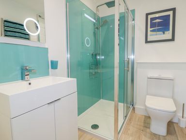 A bathroom with a white sink cabinet shower with glass doors and a toilet at Fistral Drift in Newquay